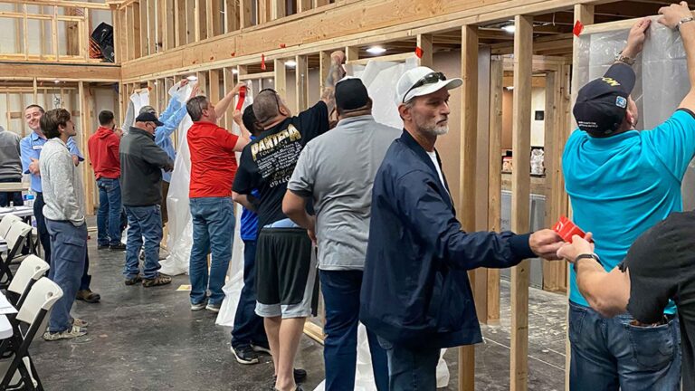 A line of adult students work together to install asbestos abatement sheeting.